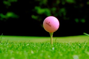 A pink golf ball on the tee in the grass.